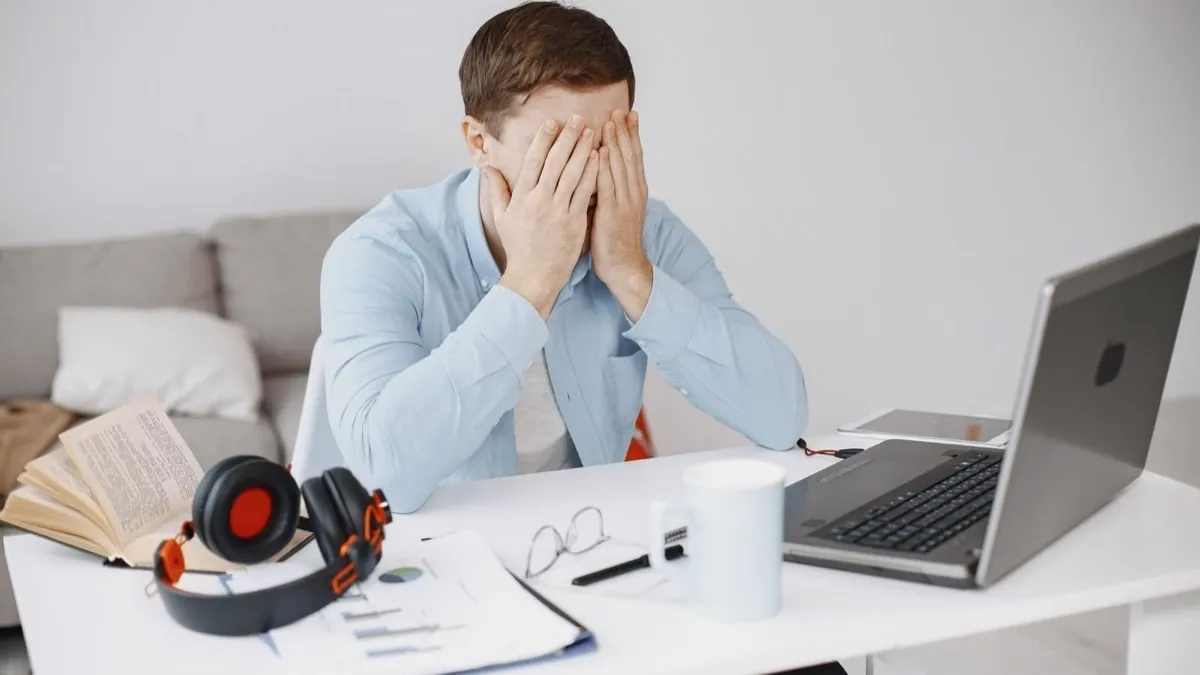 Pessoa exausta na mesa de trabalho ao lado de uma xícara de café e um laptop