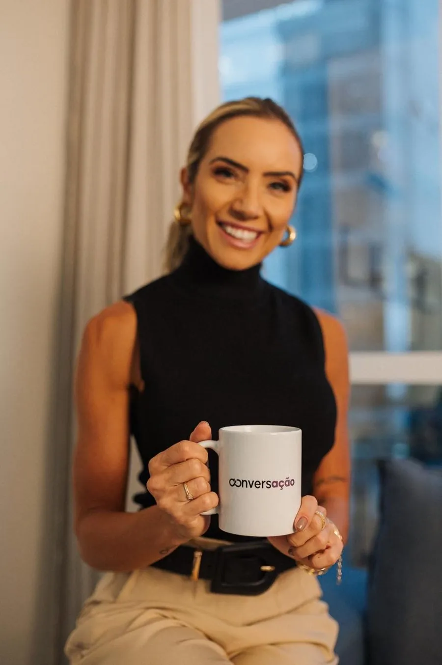 Andressa Langlois sorrindo, segurando a caneca do podcast Conversação